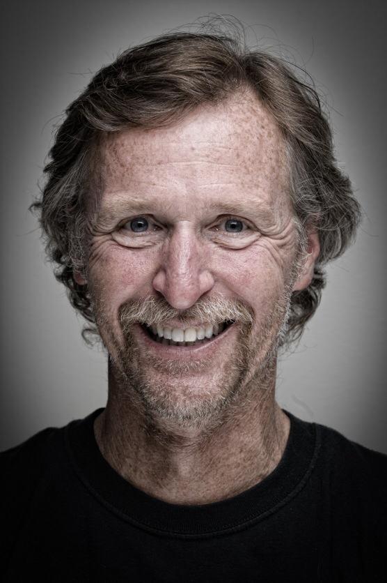 A man with long hair and a beard smiling.