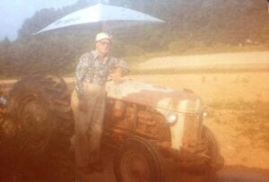 A man standing next to an old tractor with an umbrella.