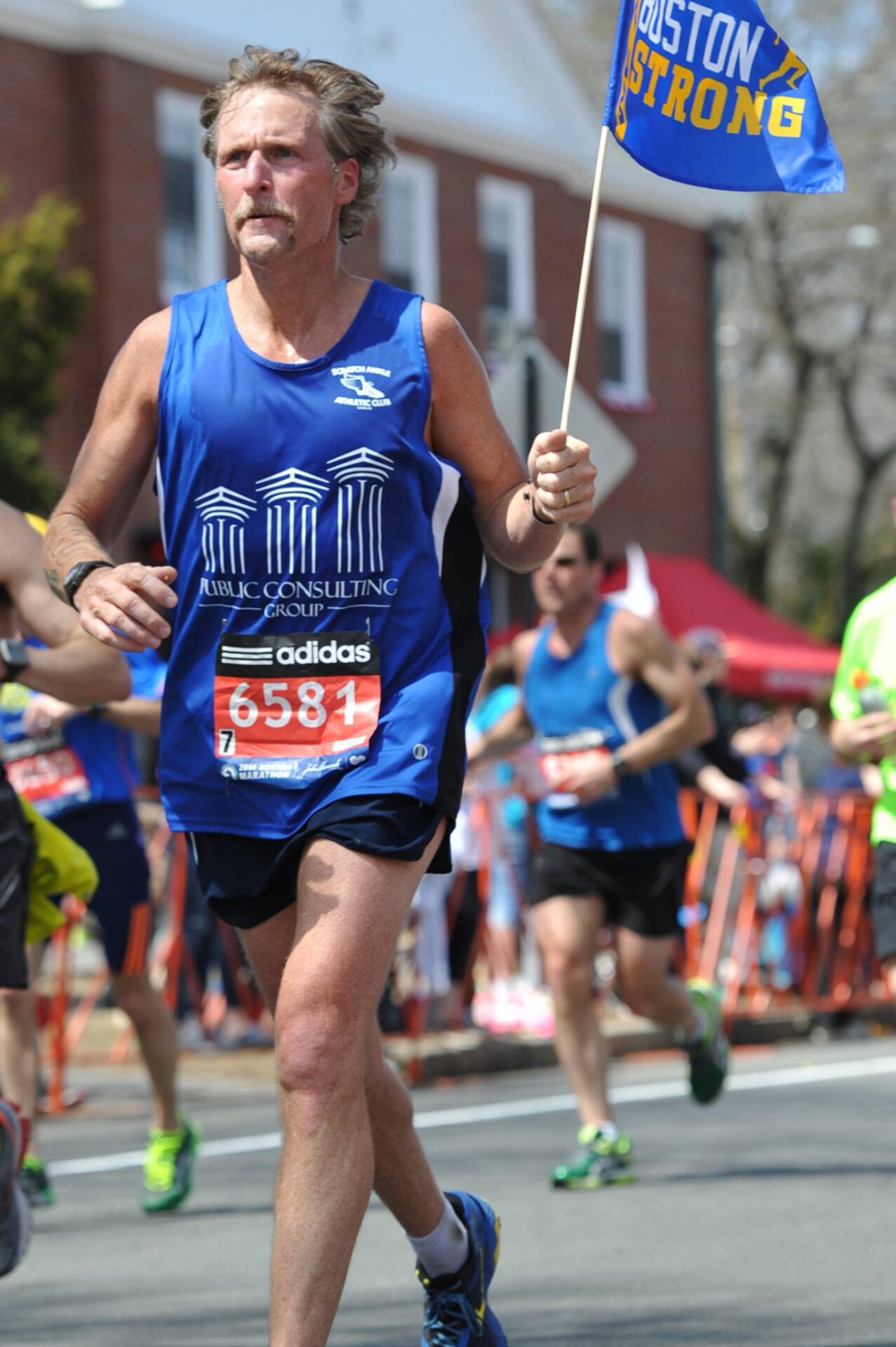 A man running in the marathon while holding onto a stick.