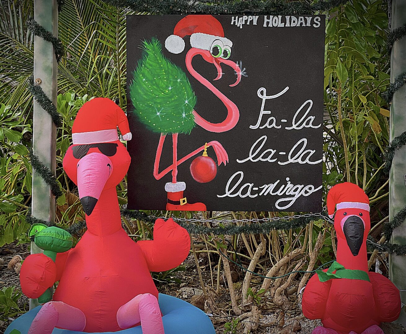 Two inflatable flamingos are sitting in front of a sign.