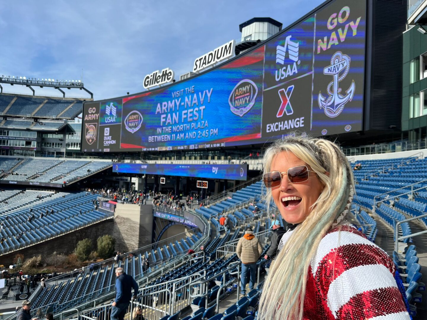 A woman in sunglasses and an american flag jacket standing at the top of a stadium.